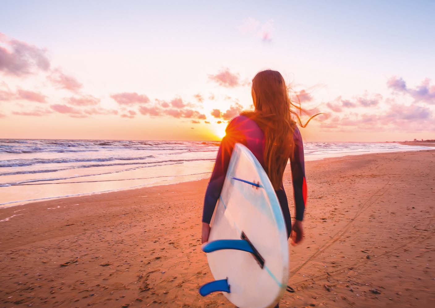 Mädchen mit Surfbrett an einem Strand in Australien bei Sonnenuntergang