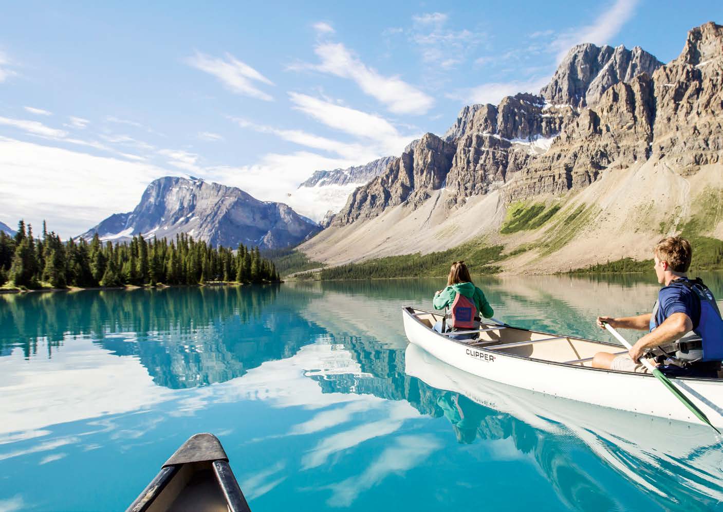 Sicht aus einem Ruderboot auf einem Bergsee im Kanada. Ruderboot mit zwei Personen rechts, Berge und Wald im Hintergrund